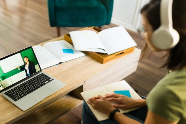 Jovem estudando online com laptop, fones de ouvido e materiais de apoio sobre a mesa