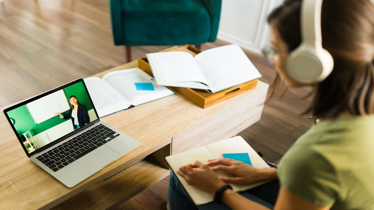 Jovem estudando online com laptop, fones de ouvido e materiais de apoio sobre a mesa